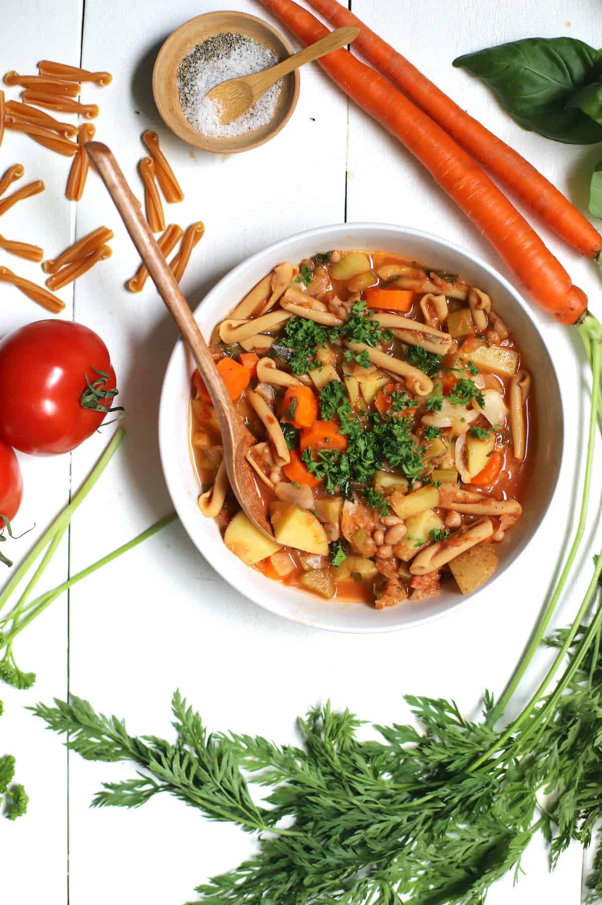 Minestrone in a white bowl with vegetables and pasta on white table.