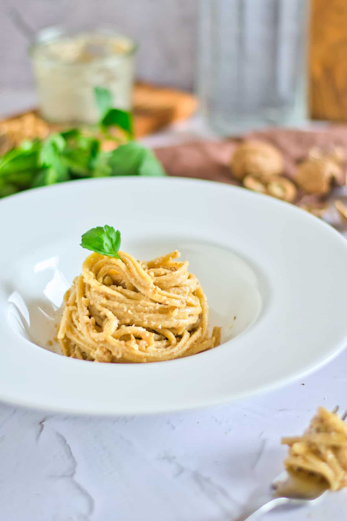 Walnut sauce with pasta topped with sprig of parsley in a white dish.