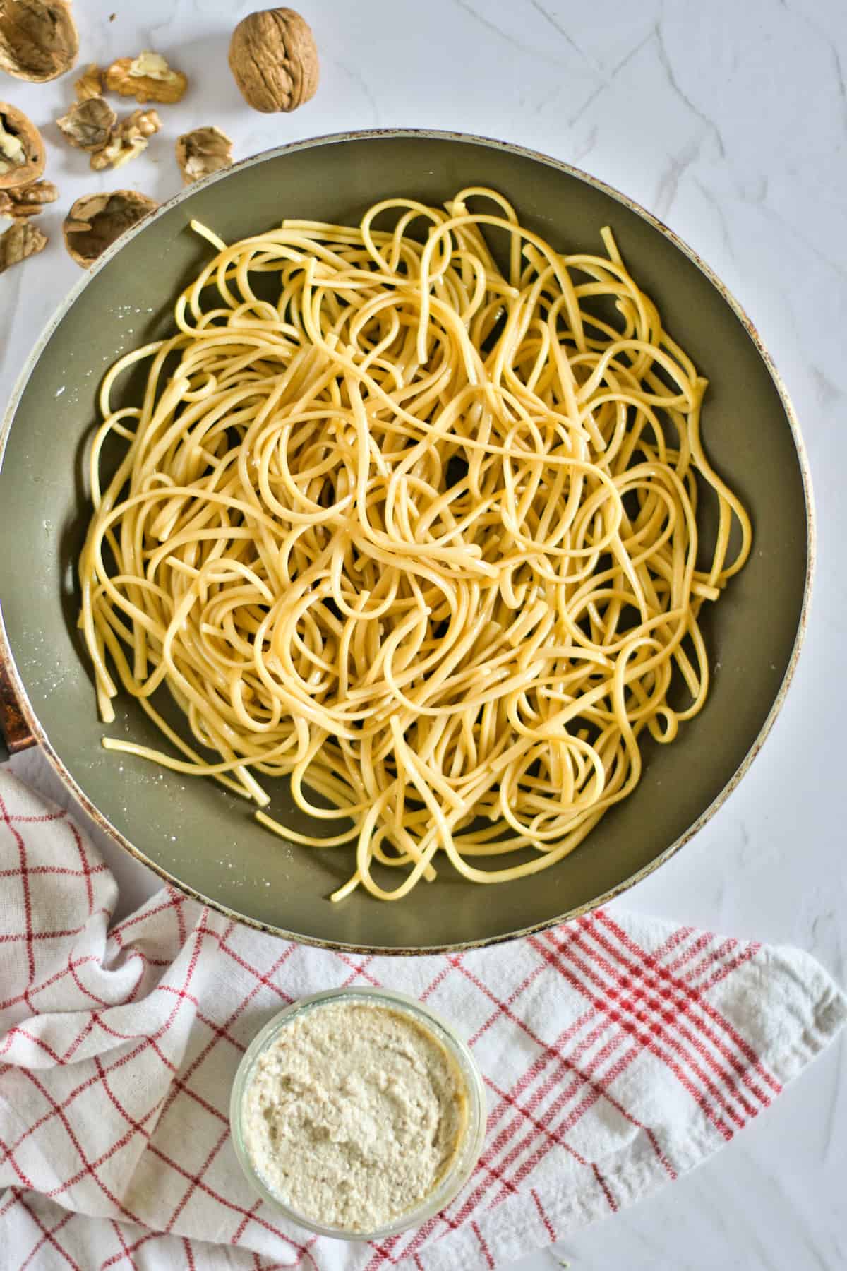 Pasta in a pan with a bowl of white sauce.
