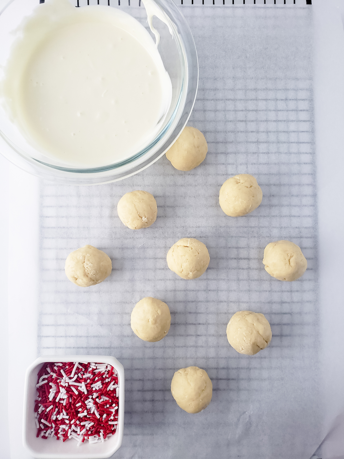 Cookie dough bites on parchment paper on a wire rack with melted white chocolate and red and white sprinkles.