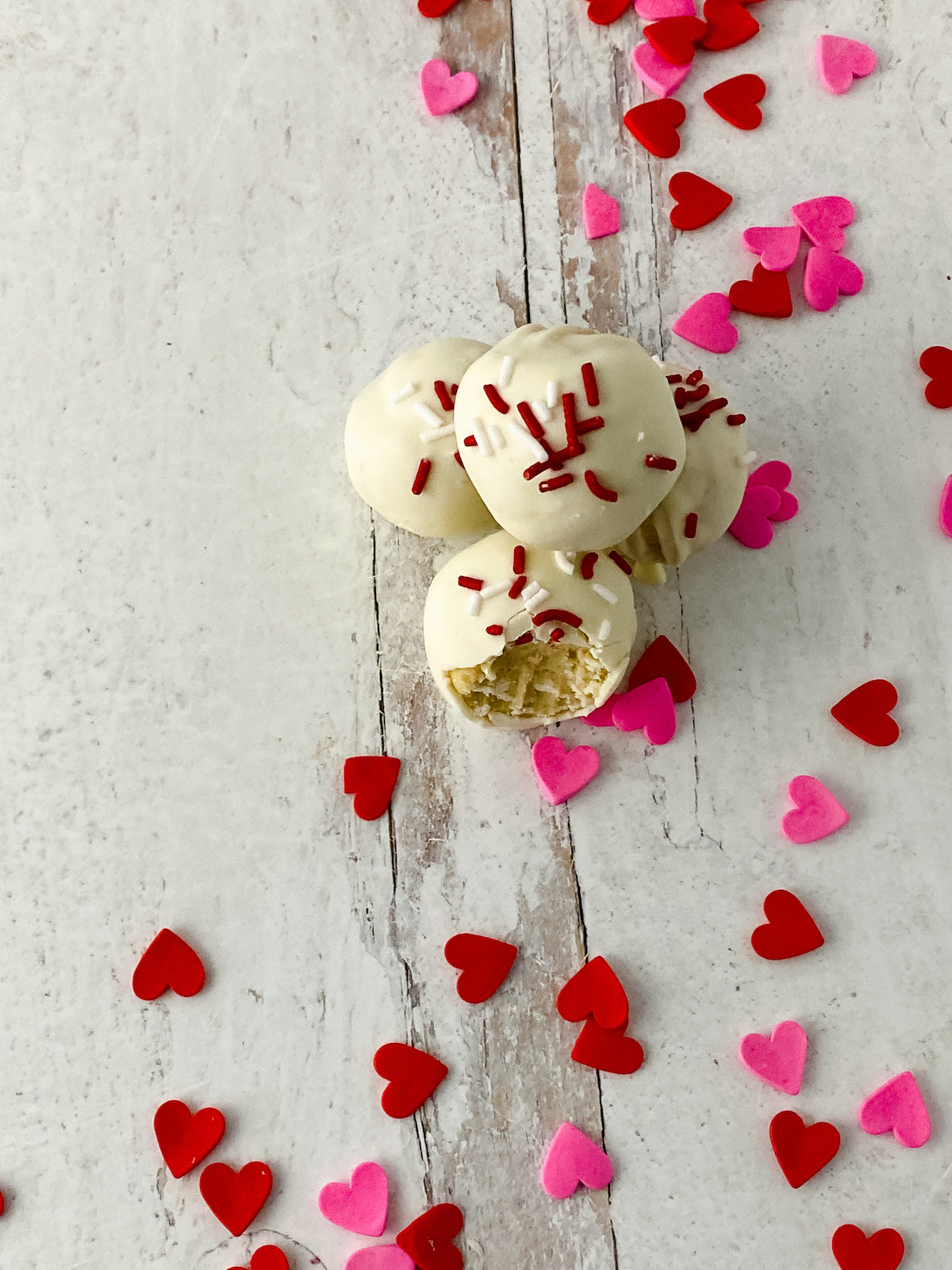 Cookie dough balls dipped in white chocolate and decorated with Valentine's Day sprinkles on a white table.