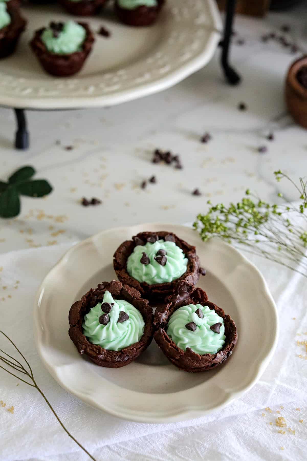 Brownie bites with light green filling with chocolate chips on a white plate on a white tabelcloth.
