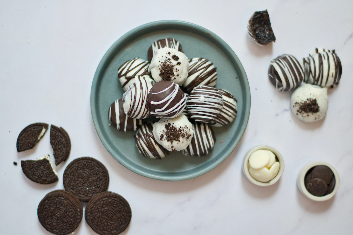 OREO Cake Balls on a teal plate on a white table with OREO cookies and more cake balls on the side.