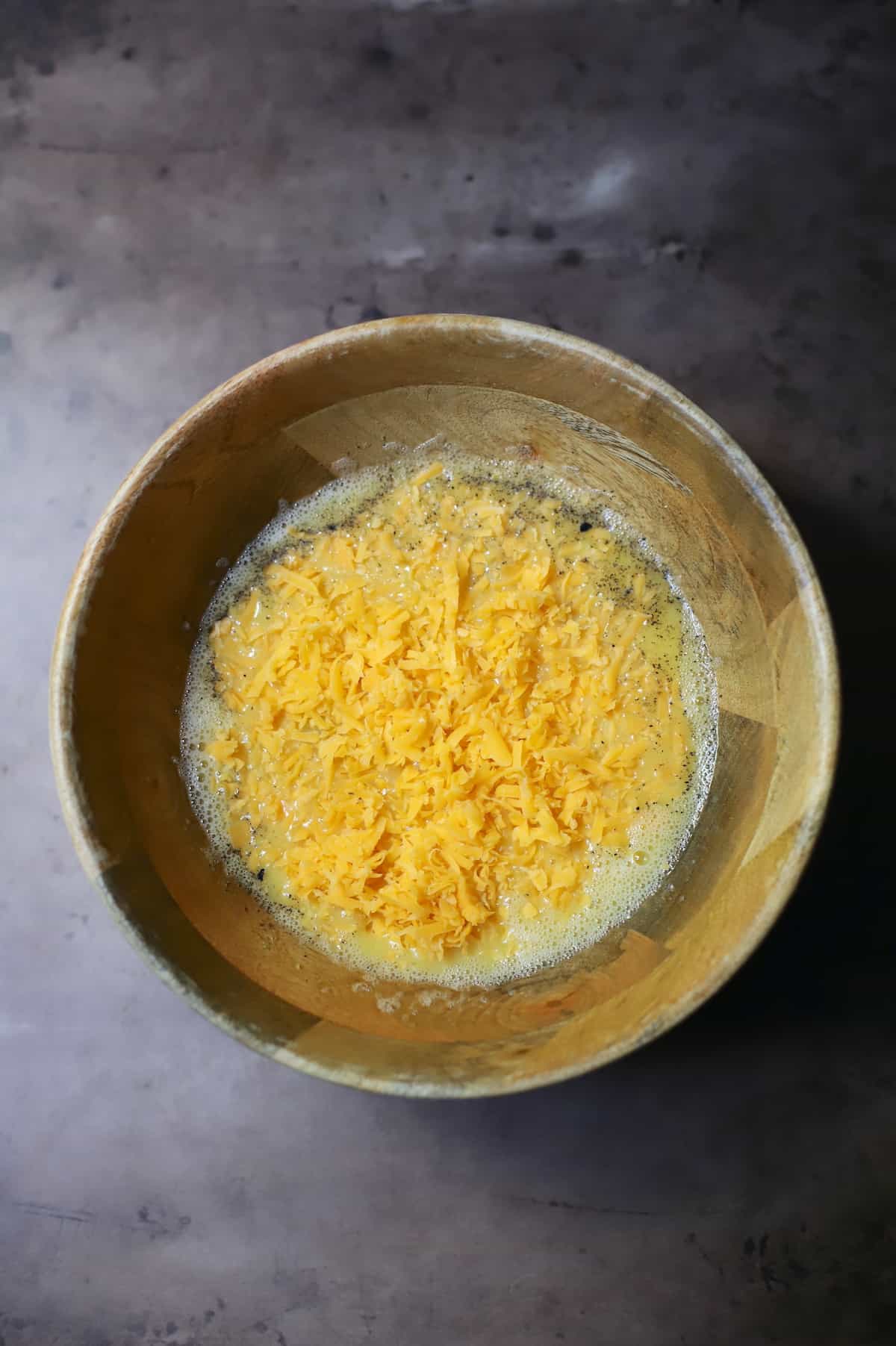 Eggs, hash browns, cheese, salt and pepper in a wood bowl.