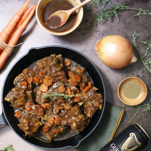 Guinness braised short ribs in a cast iron skillet with onion, gravy, celery seed, thyme, and carrots.