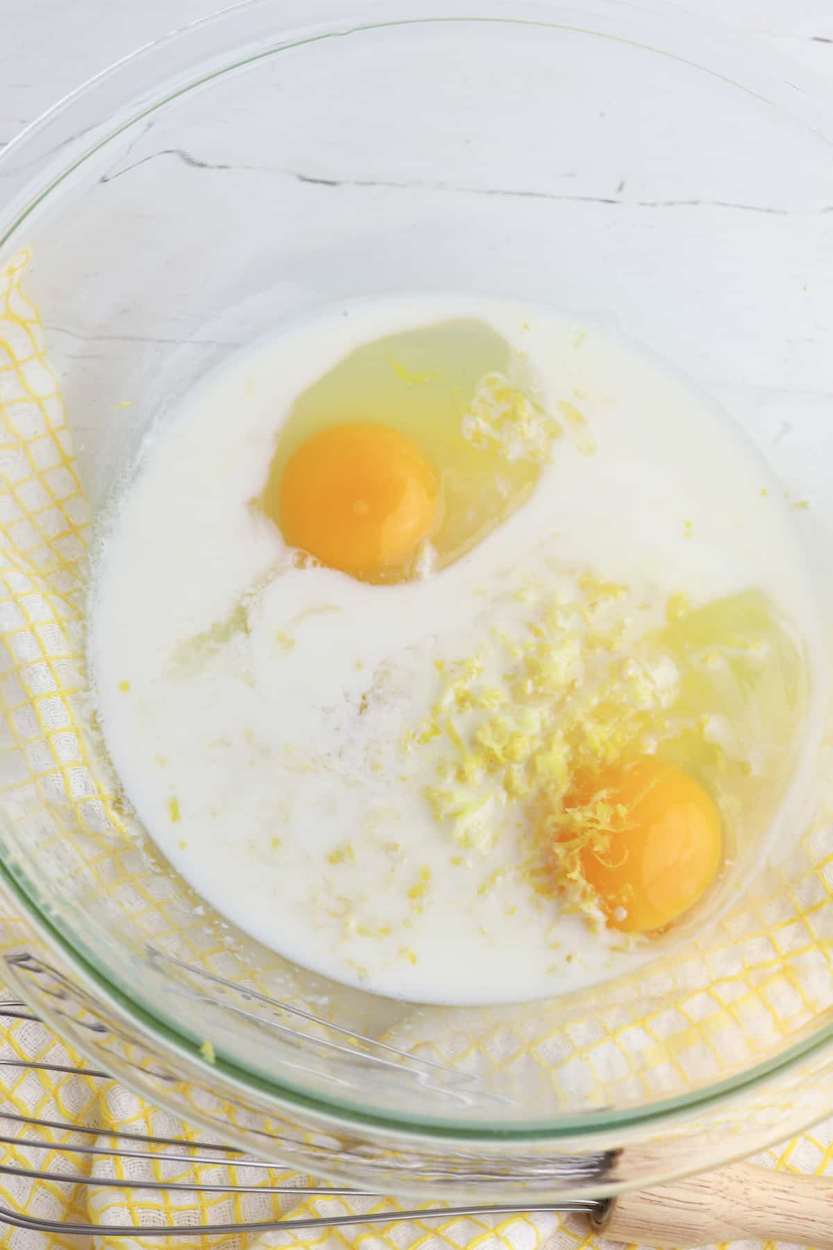 Sugar, eggs, lemon extract, lemon zest, lemon juice, and milk in a glass bowl.