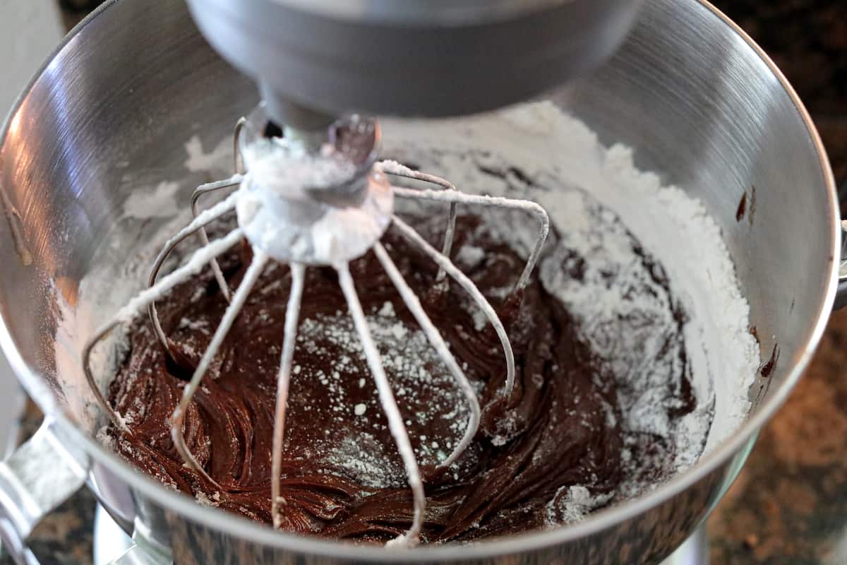 Chocolate brownie batter with sugar in stand mixing bowl.