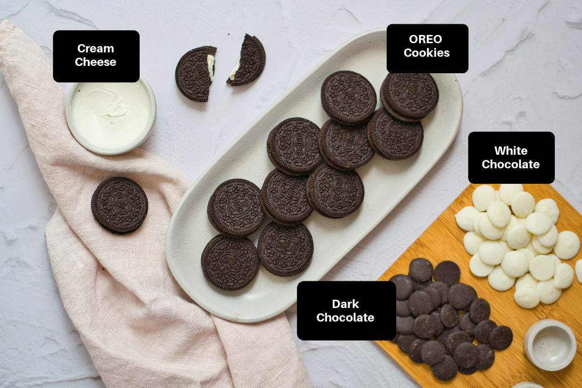OREO cookies on a white plate, white and dark chocolate wafers on cutting board, and cream cheese in a bowl.