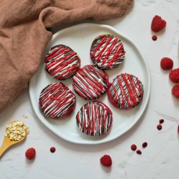 Raspberry filled cookies on a white plate on a white table with bowl of raspberries.