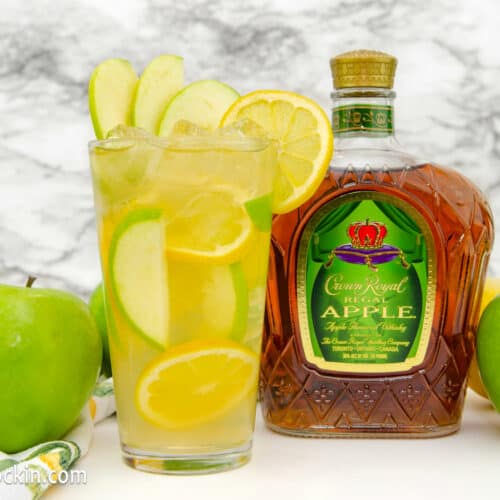 Crown Apple and Lemonade cocktail on a shite table with bottle of Crown Royal Apple and apples.
