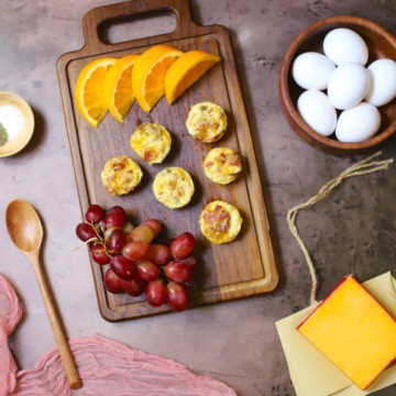 Egg bites on a wooden cutting board with oranges and grapes.