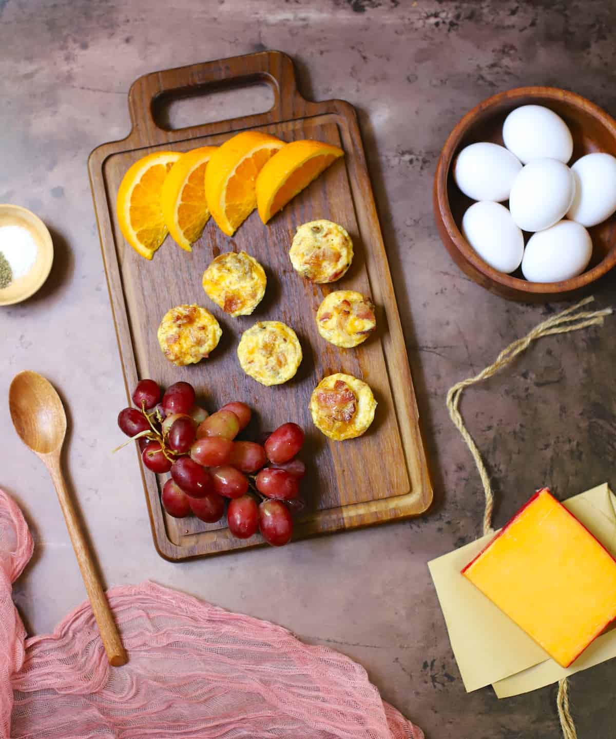 Egg bites on a wooden cutting board with oranges and grapes.