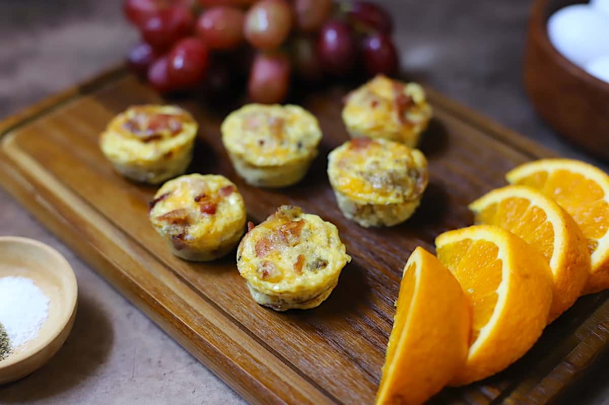 Egg bites on a wooden cutting board with oranges and grapes.