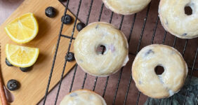 Iced baked blueberry cake donuts on a wire rack with lemons and blueberries on the side.