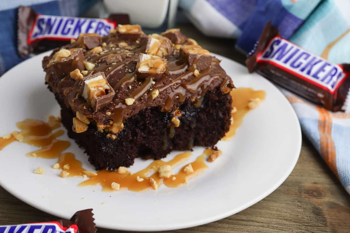 Slice of chocolate cake with frosting and chopped Snicker's bars.