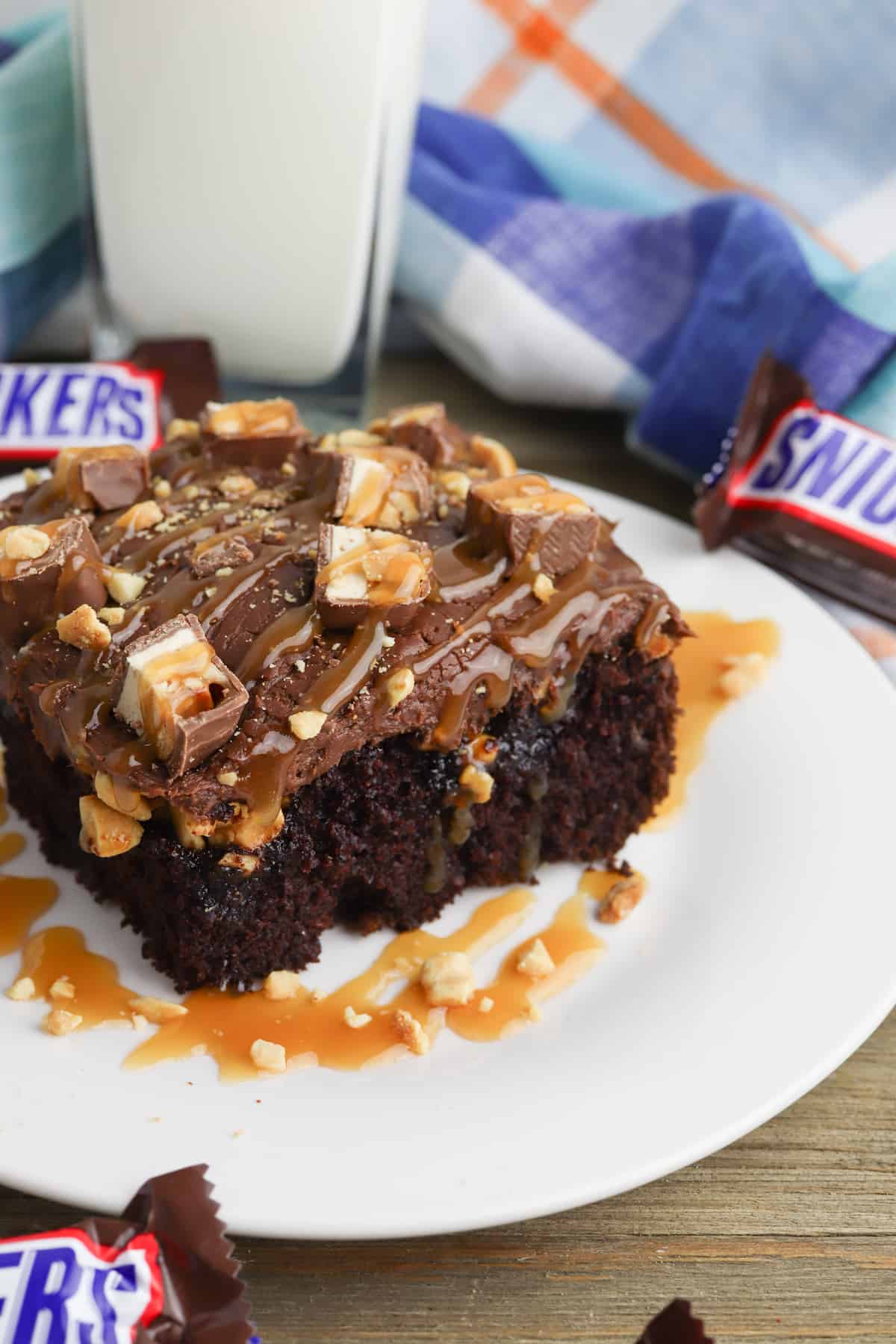 Slice of Easy Snickers Poke Cake on a white plate with Snickers bar.