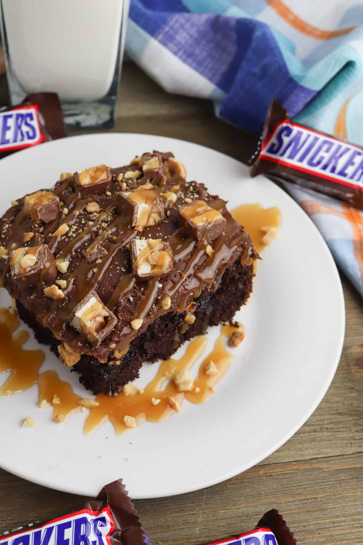 Slice of chocolate cake with frosting and chopped Snicker's bars.