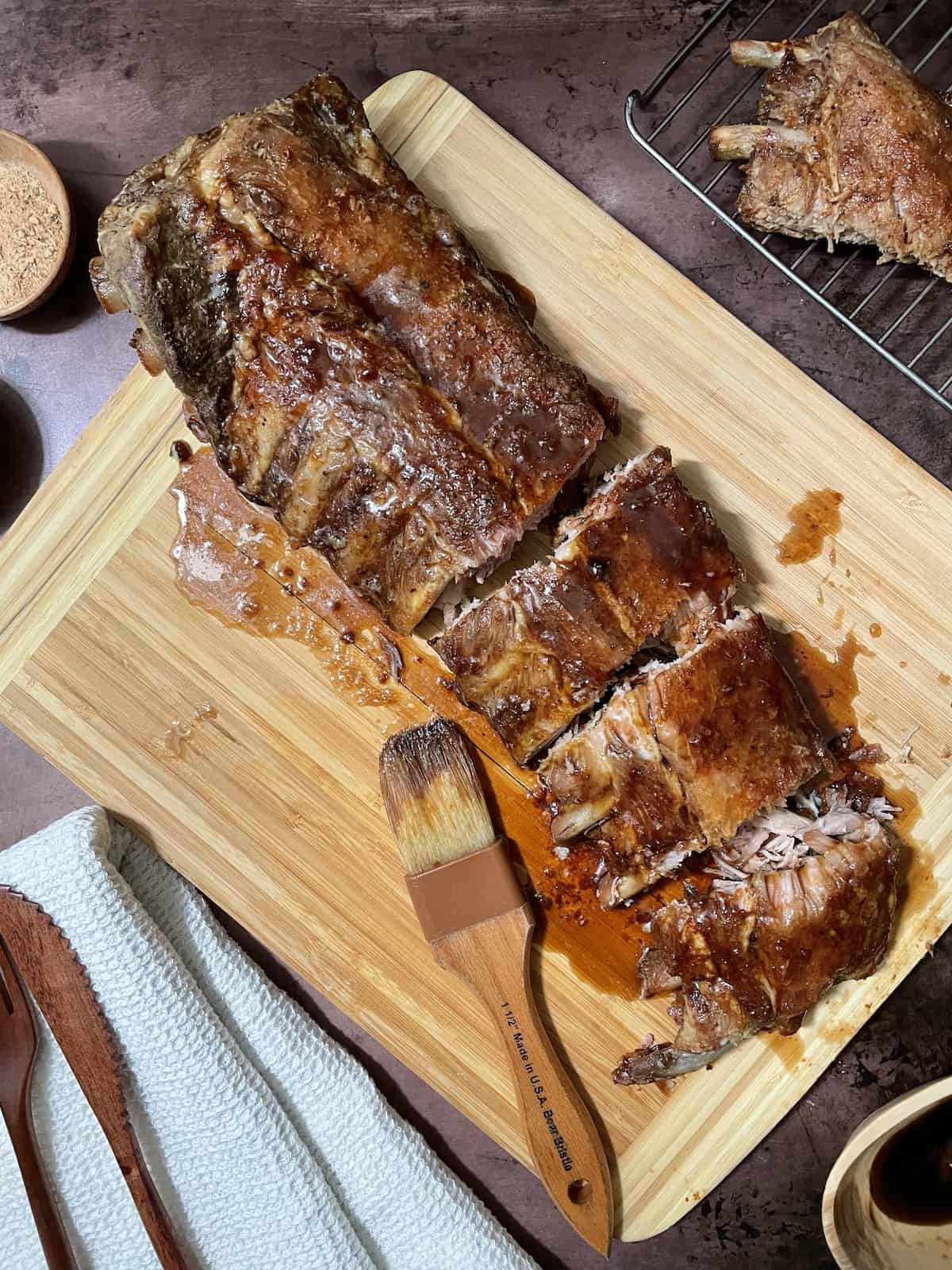 Guinness spare ribs with sauce on a wood cutting board with seasoning and sauce on the side.