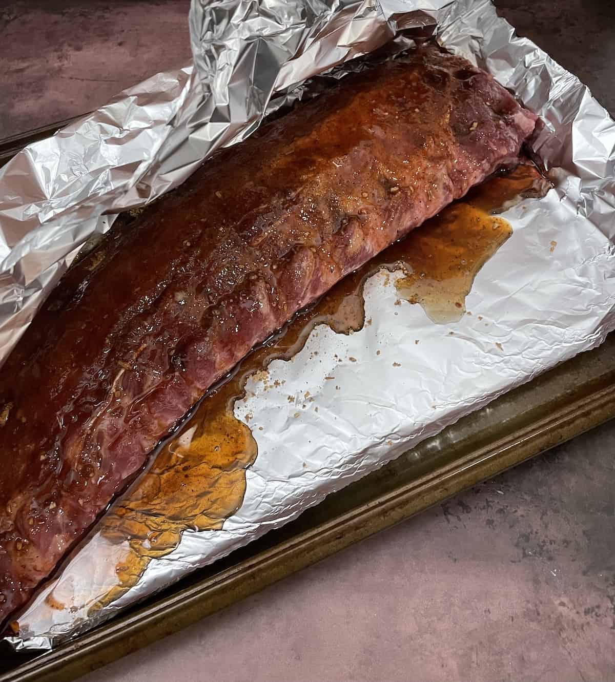 Ribs with seasoning and sauce on foil on baking sheet.