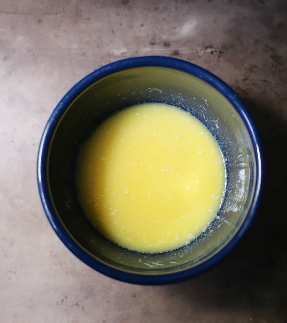 Sugar, eggs, vanilla, lemon juice, and milk in a blue bowl on a table.