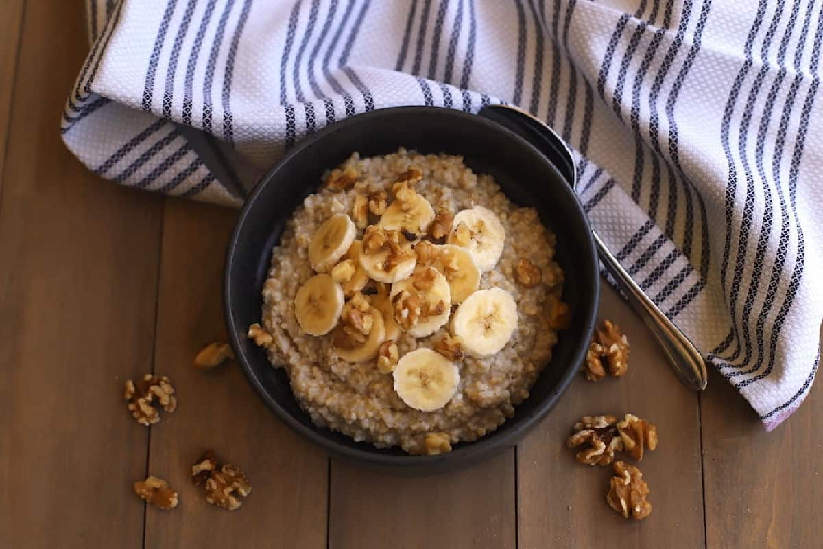 Banana nut oatmeal in a black bowl on a brown table with a striped cloth napkin.