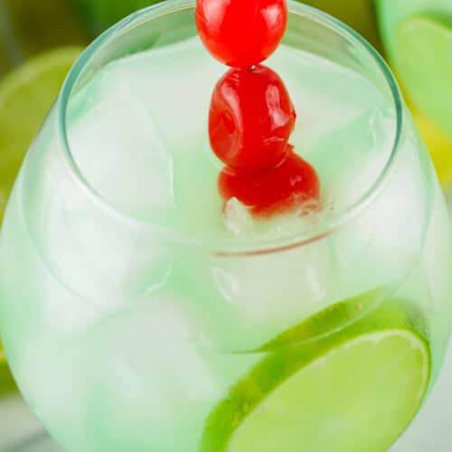Green cocktail on the rocks with cherries and lime slice.