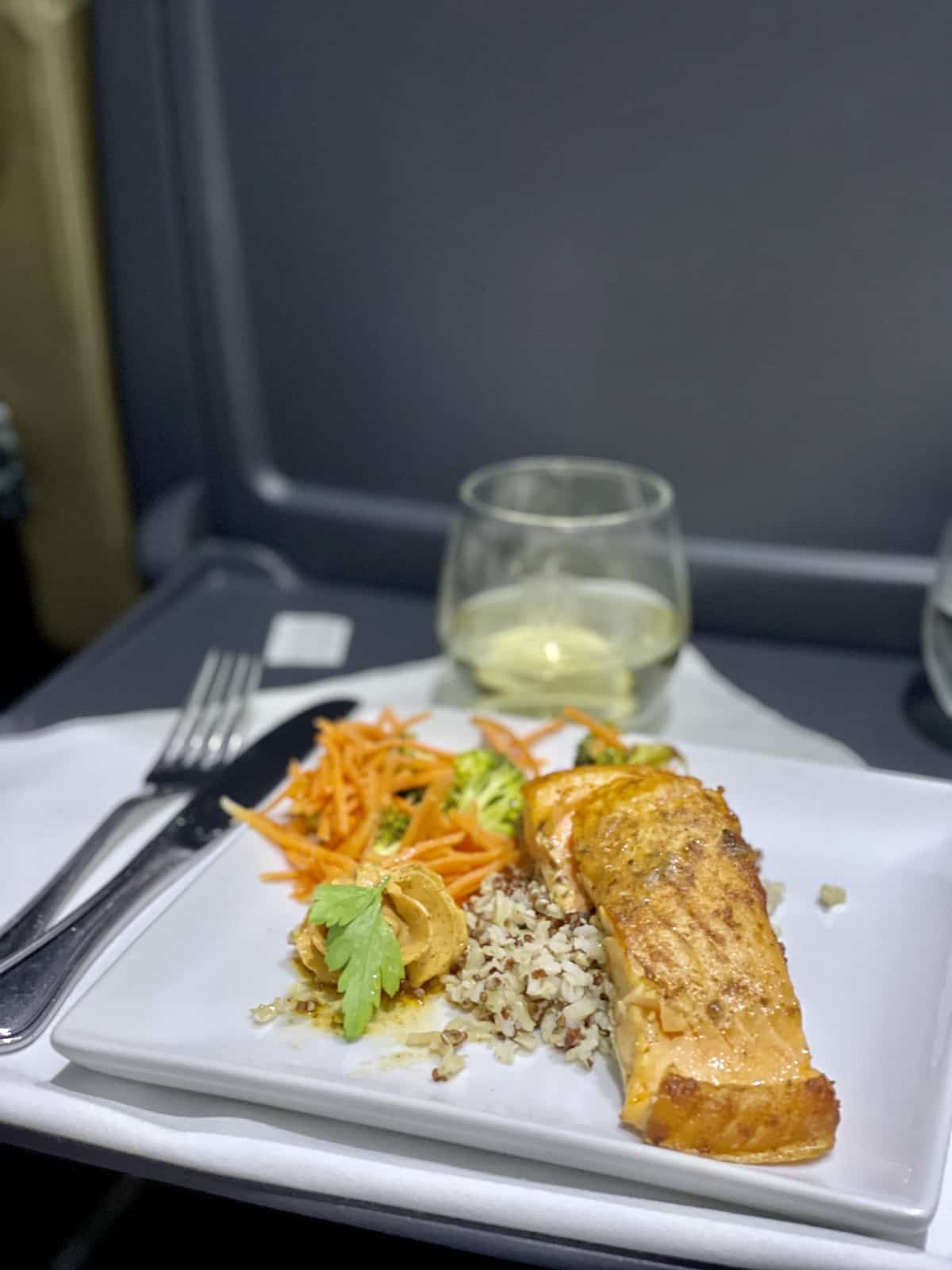 Salmon and rice with vegetables on a white plate on a white napkin with white wine in back.