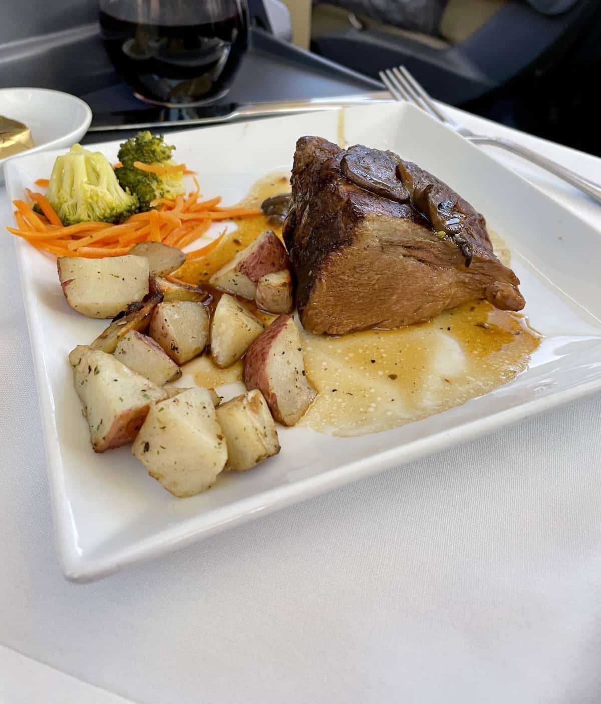 Short ribs with potatoes and vegetables on a white plate on a white napkin.