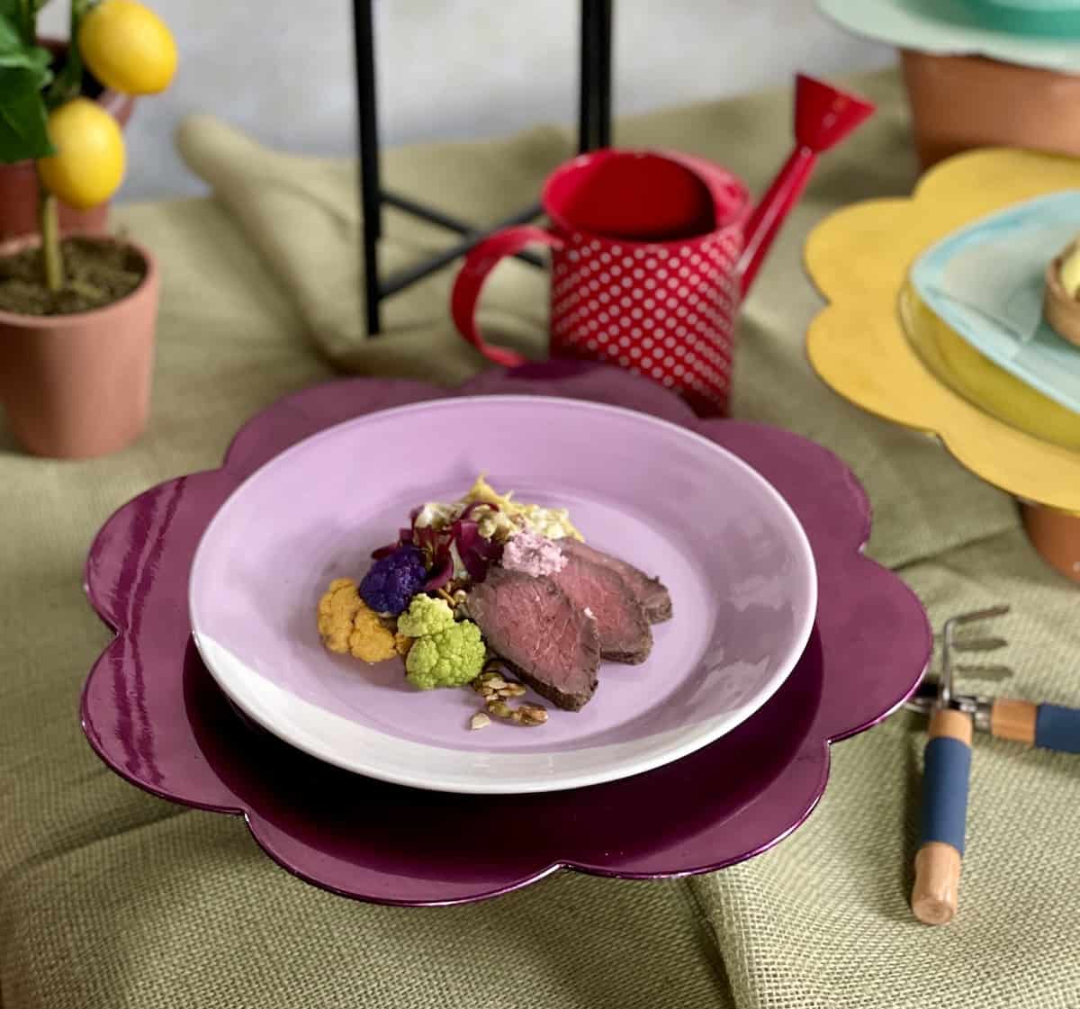 Rib eye with leek fondue on a purple plate.