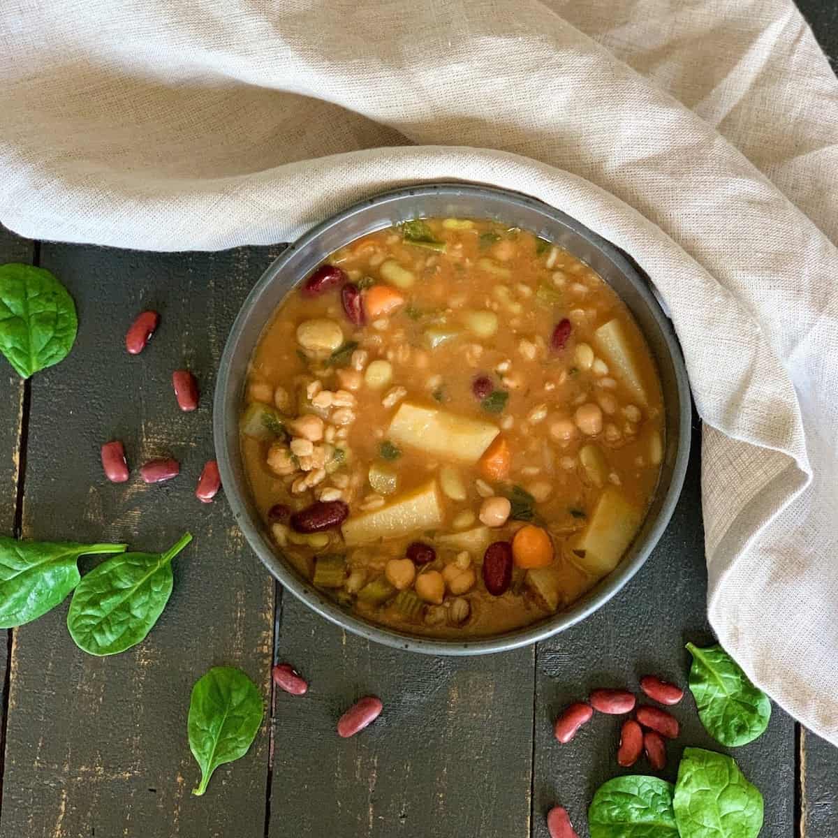Bowl of bean soup on a black table with basil and beans on table.