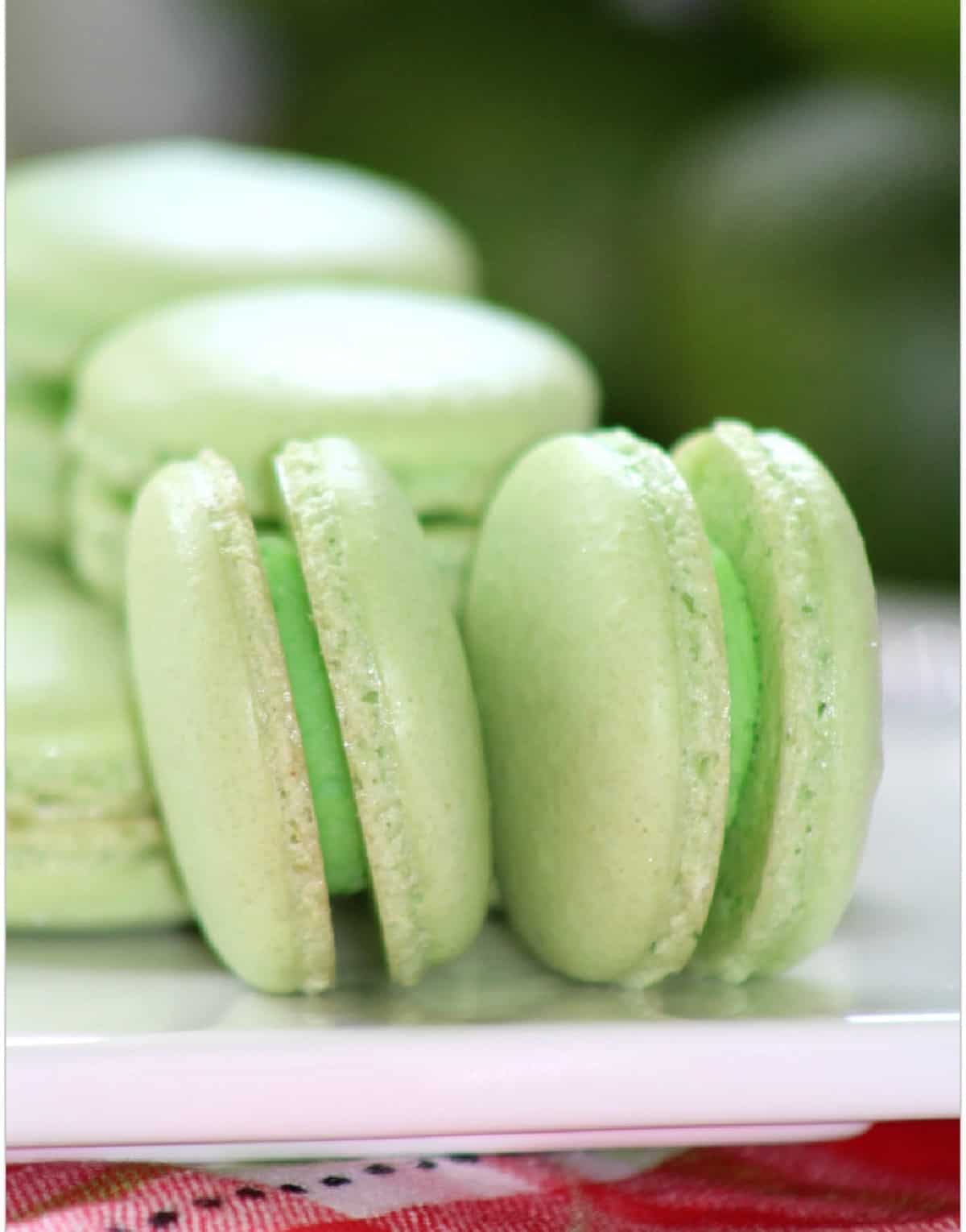 Green macarons on side on white plate on red plaid tablecloth.