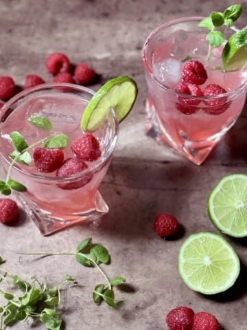 Raspberry Mojito cocktails on a table with lime, raspberries, and mint.