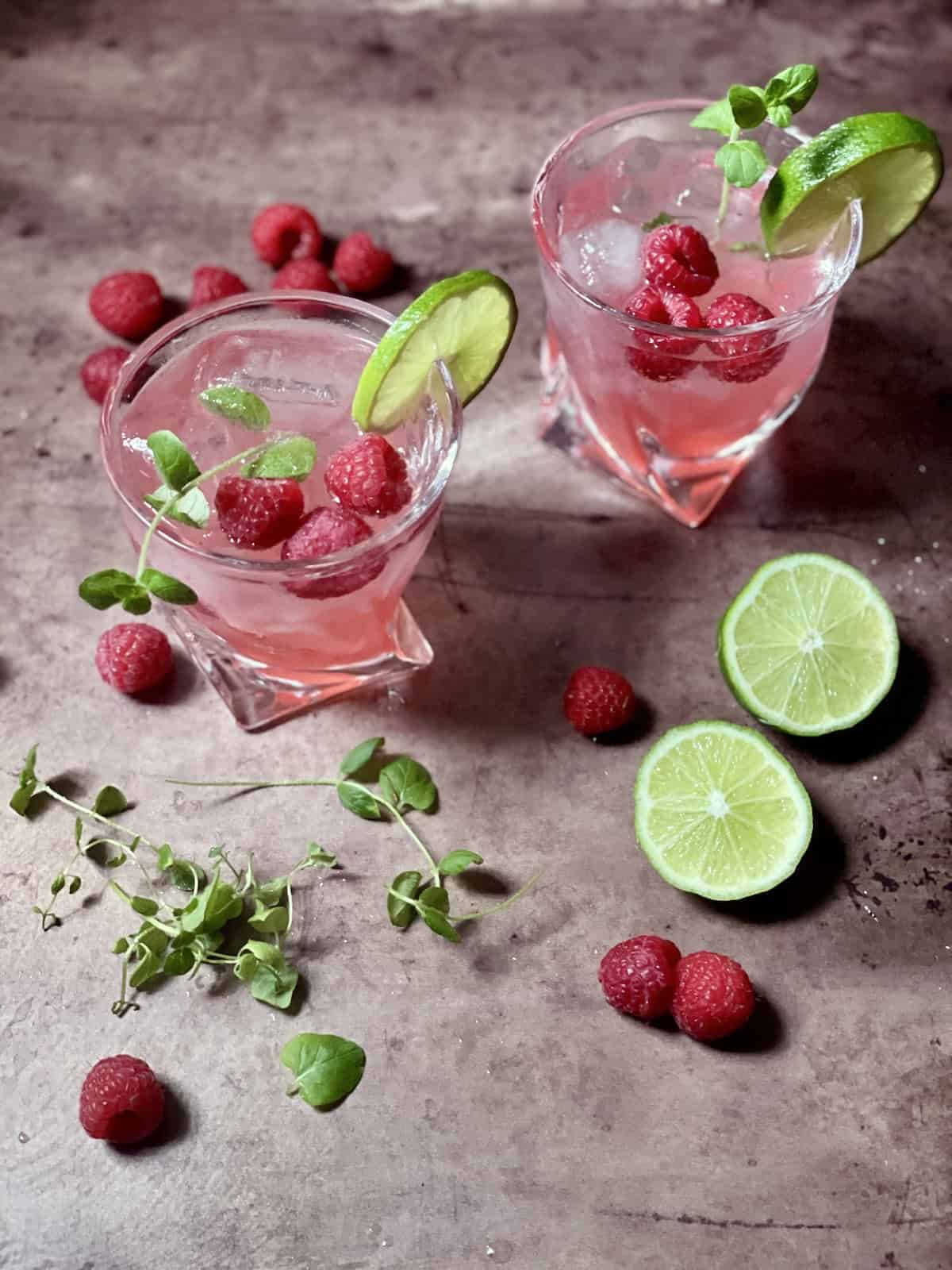 2 Raspberry Mojito cocktails on a table with raspberries, mint, and lime.