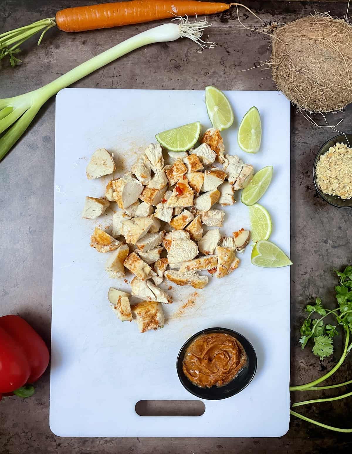Cooked chicken cut into bite-sized pieces on a white cutting board with peanut sauce.