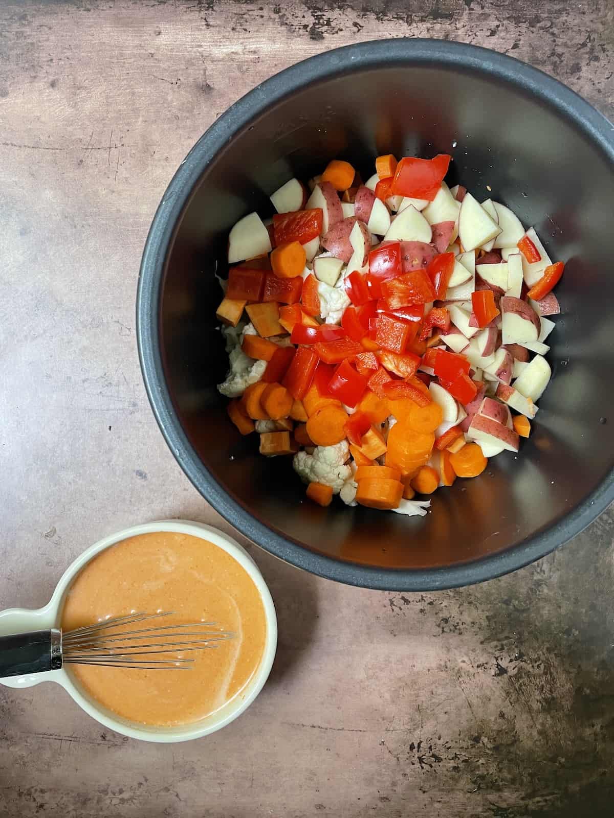 Vegetables in a slow cooker pot with sauce on side.