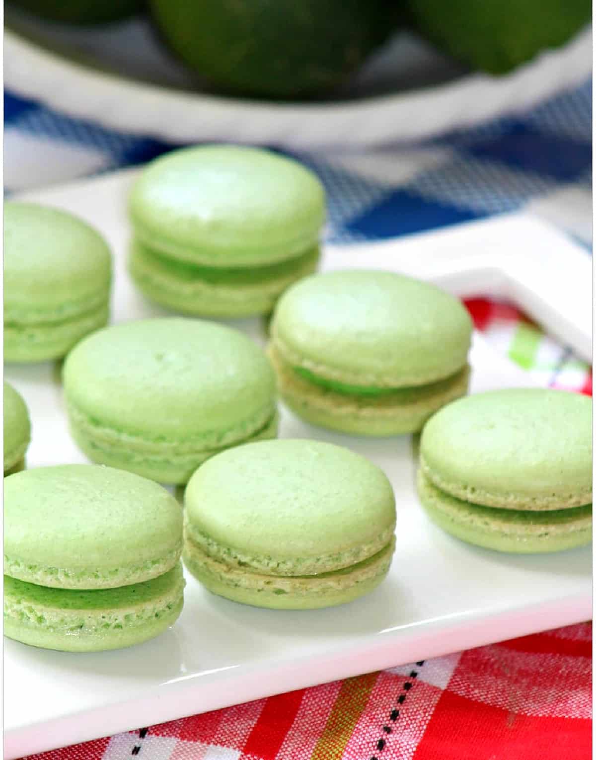 Green macaron cookies on a white plate on a red plaid tabelcloth.
