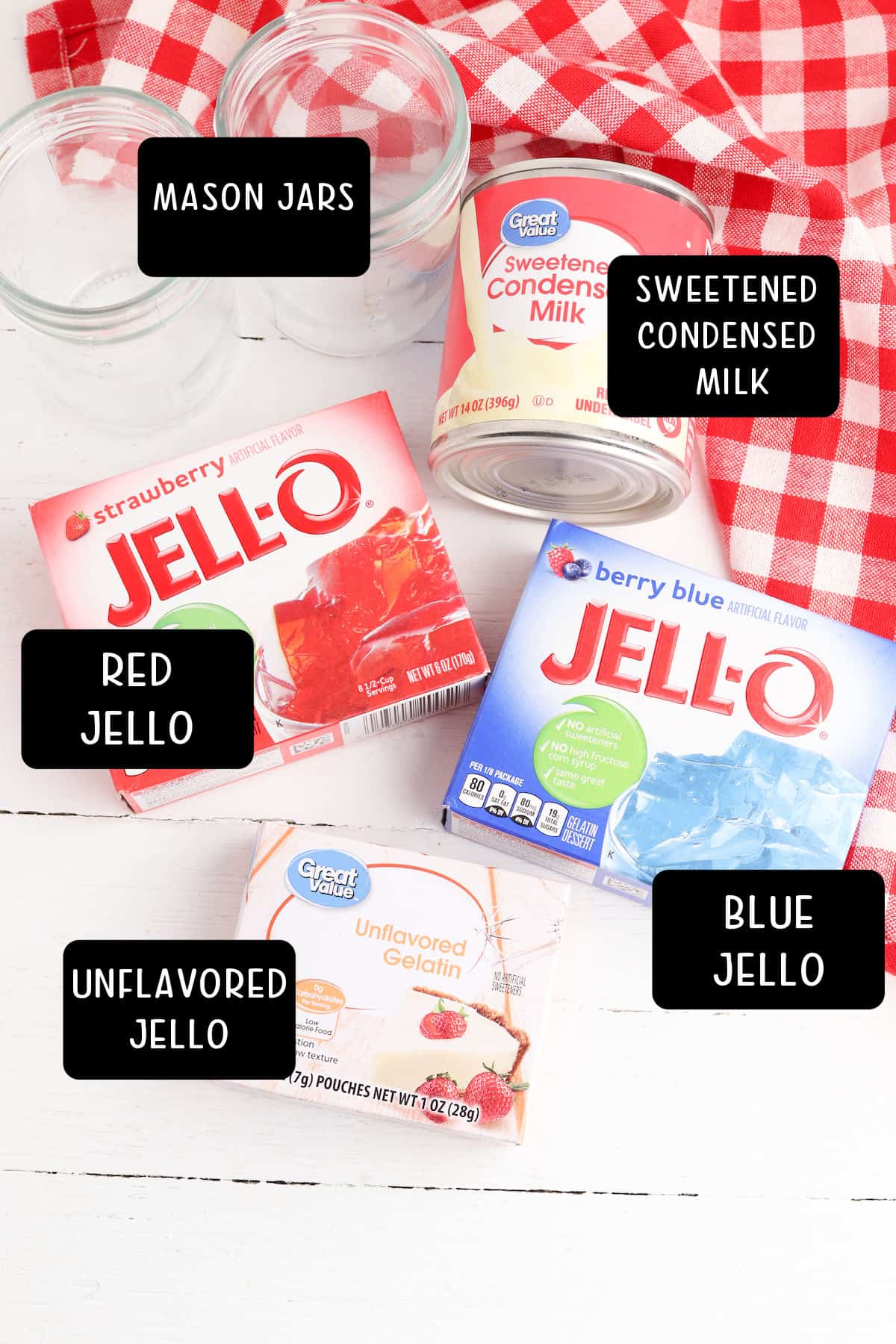 Boxes of jello, can of condensed milk, mason jars, on a white table with a red and white checked napkin.