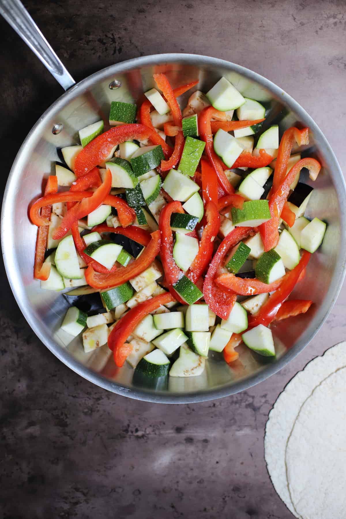 Raw vegetables in aluminum pan with tortillas on side.