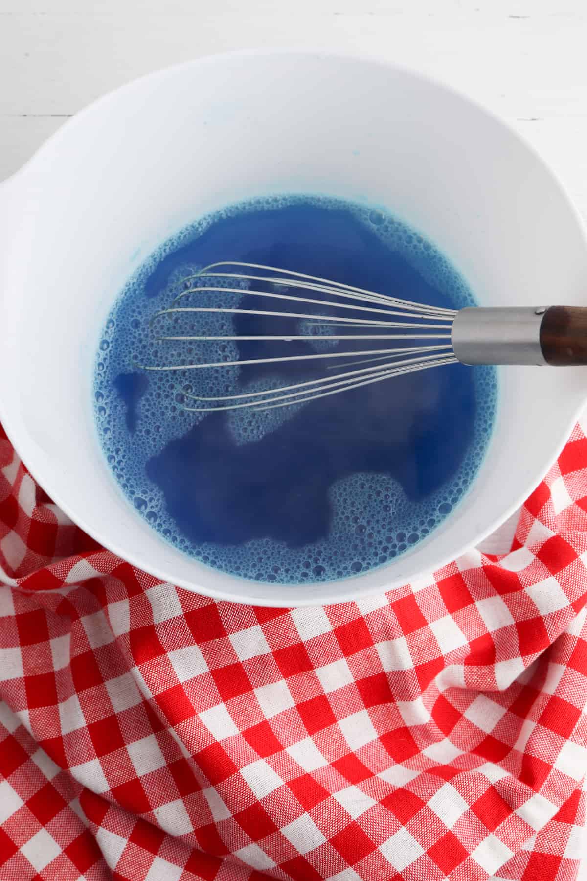 Blue jello in white bowl on red and white checked napkin.