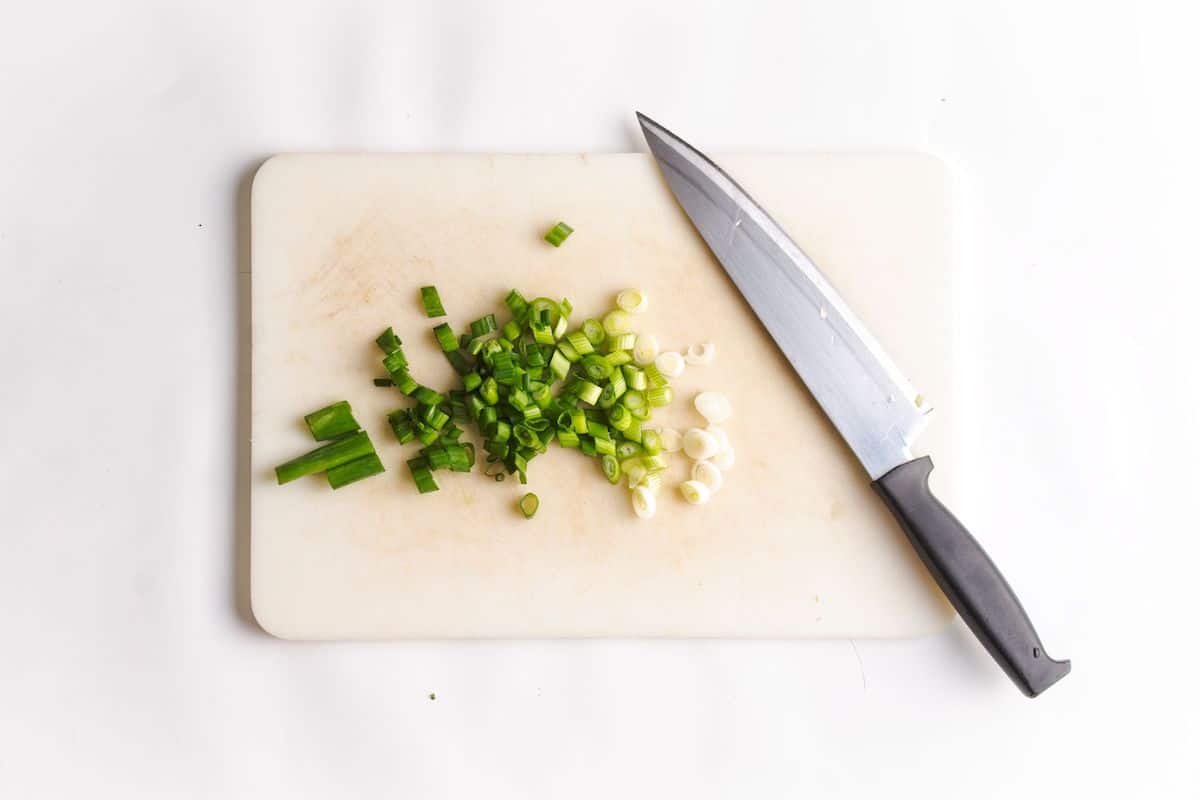 Slice green onions on cutting board with knife.