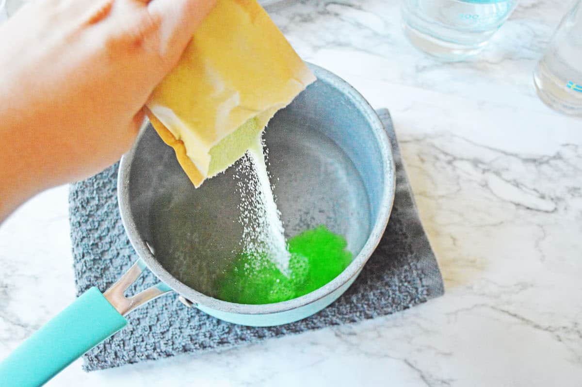 Green jello in sauce pan with water on blue towel.