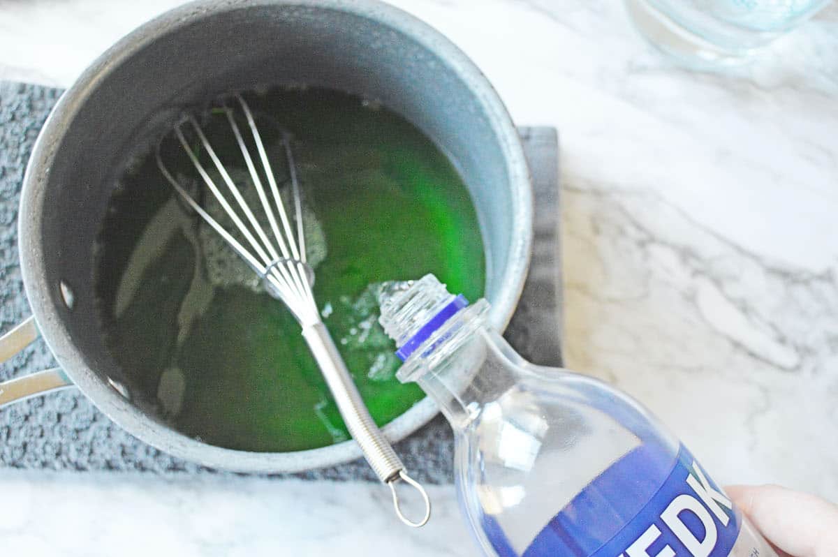 Adding vodka to green jello in sauce pan.