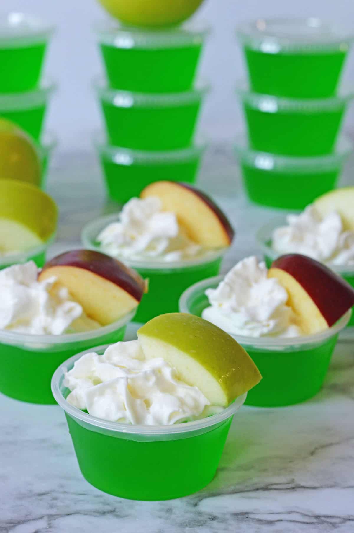Apple jello shots with whipped cream and apple slice.