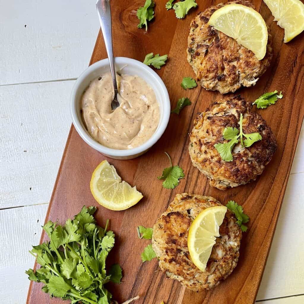 Crab Cakes on a wood board with lemon slices, parsley, and sauce.