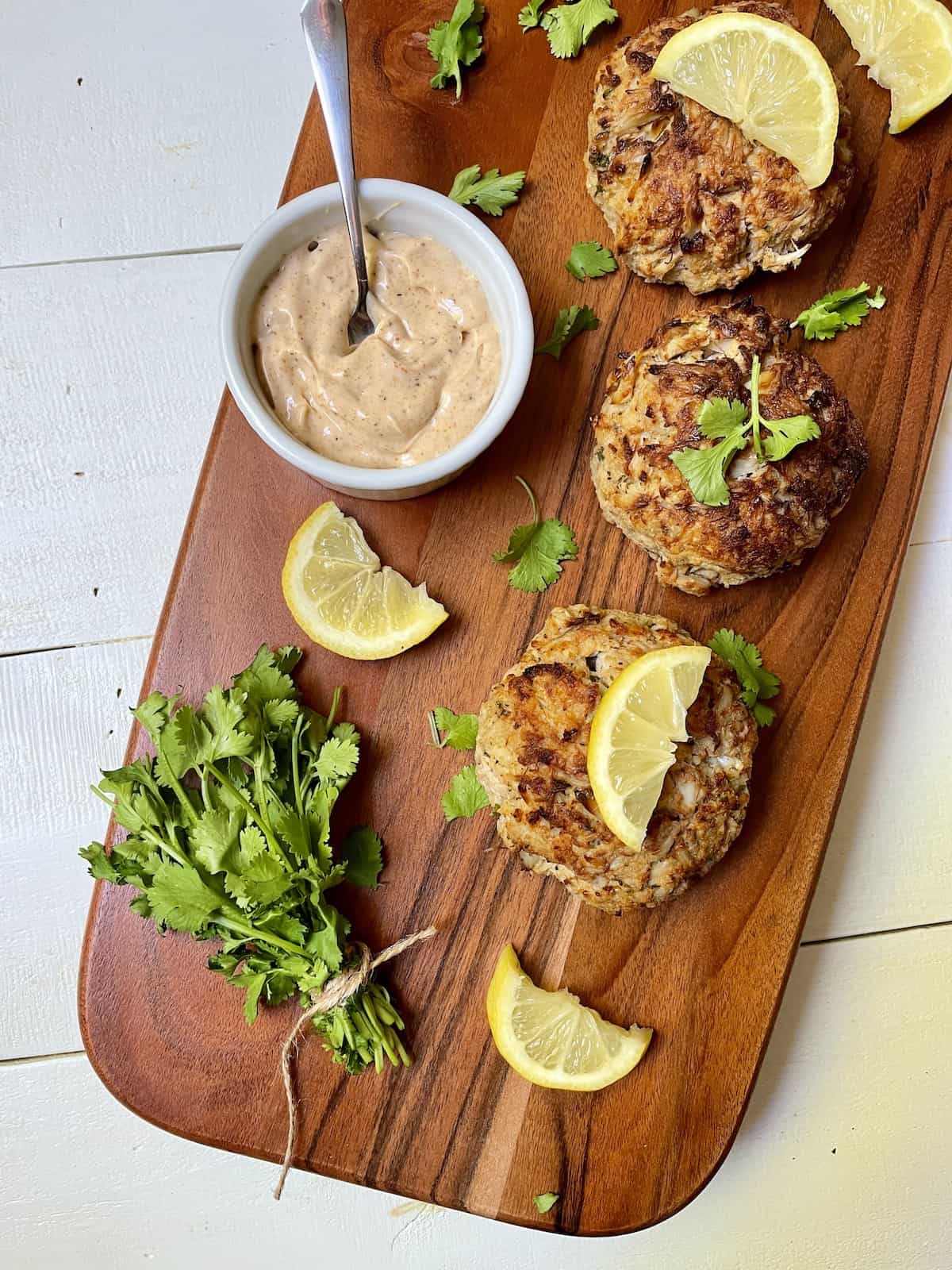 Crab cakes with lemon and parsley on a wood board.