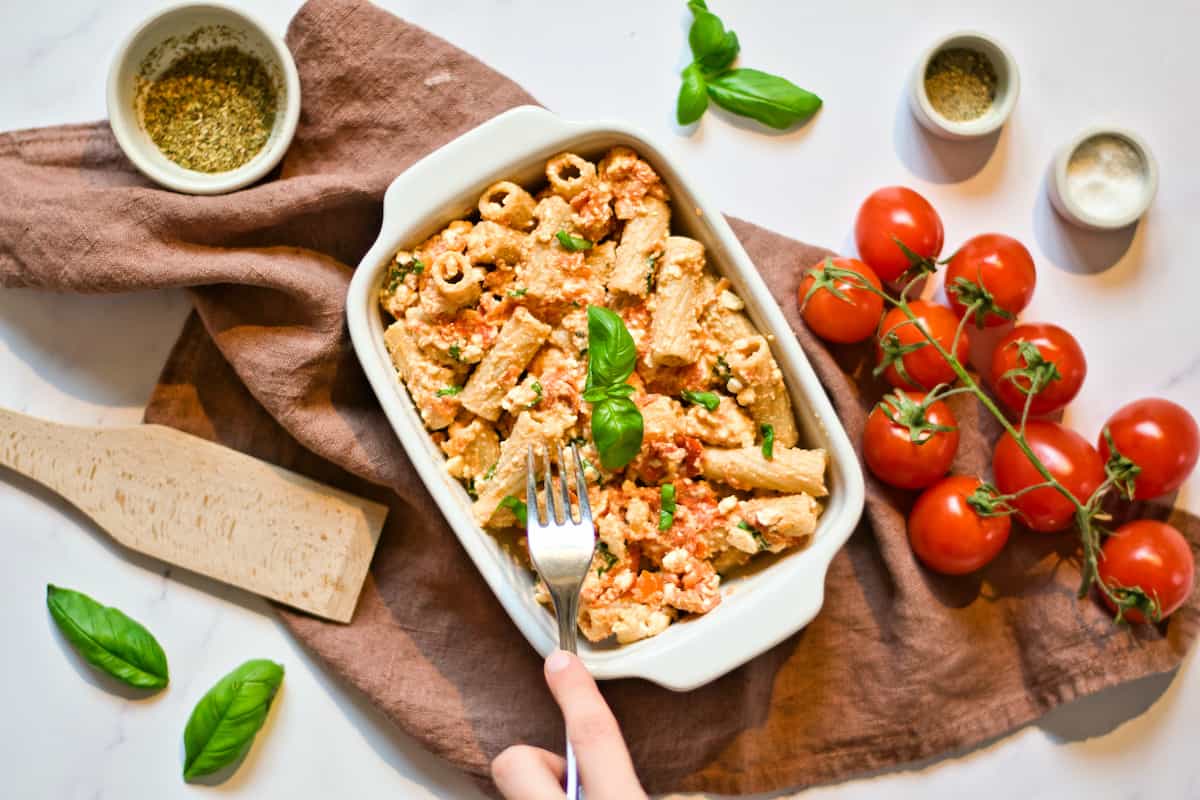 Cooked feta, tomatoes, and pasta in white dish with basil.