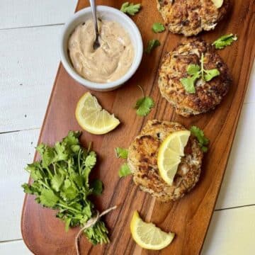 Crab cakes with lemon, parsley, and sauce on a wood board.