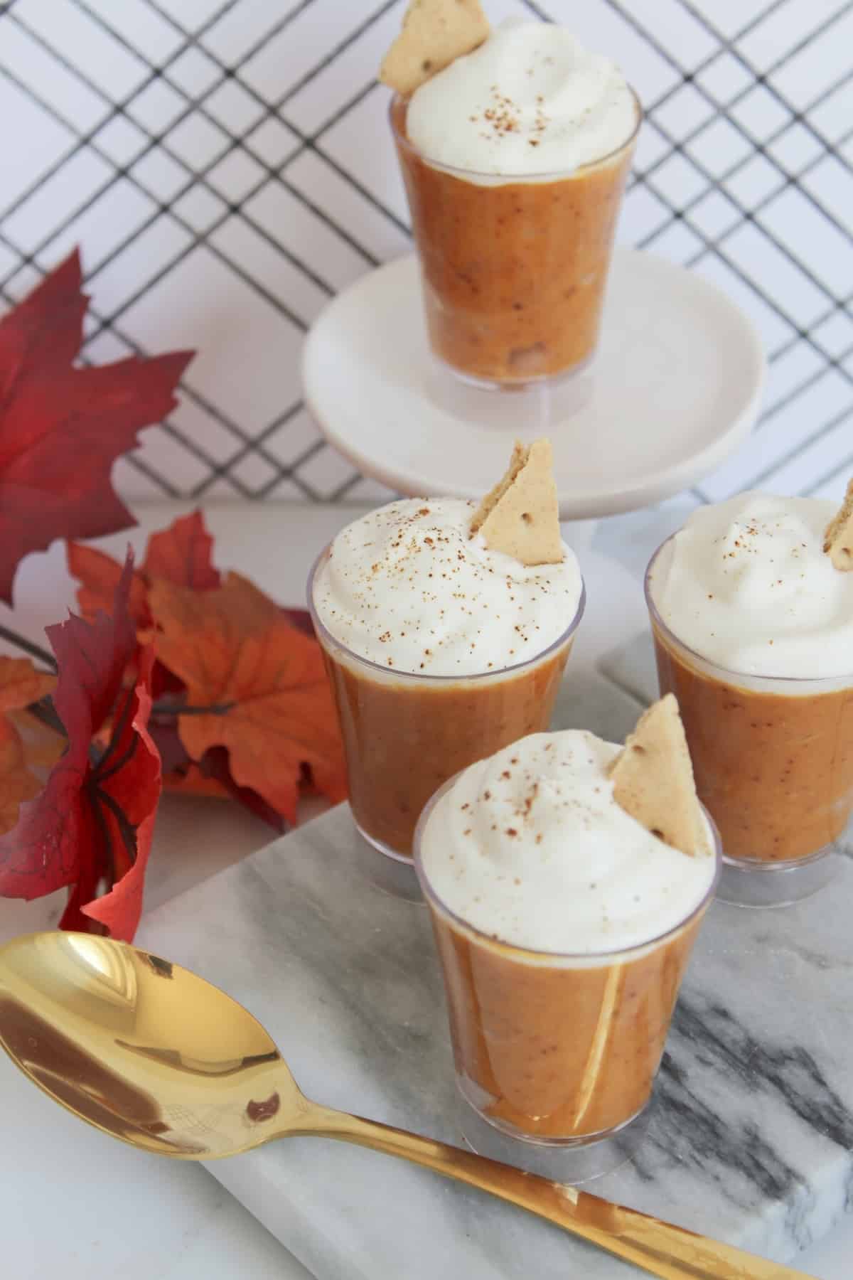 Pumpkin pudding in shot glasses with whipped cream in marble board with gold spoon.
