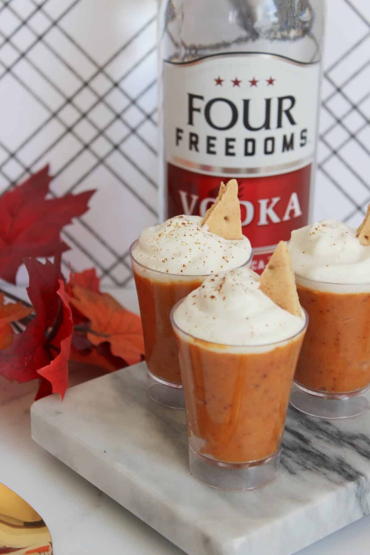 Pumpkin pudding cups with whipped cream in front of bottle of vodka.