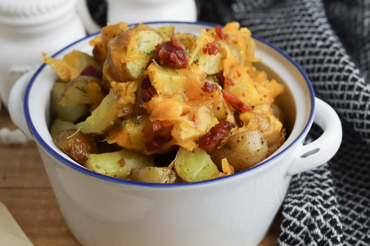 Roasted potatoes with cheese and bacon in a crock on a table.